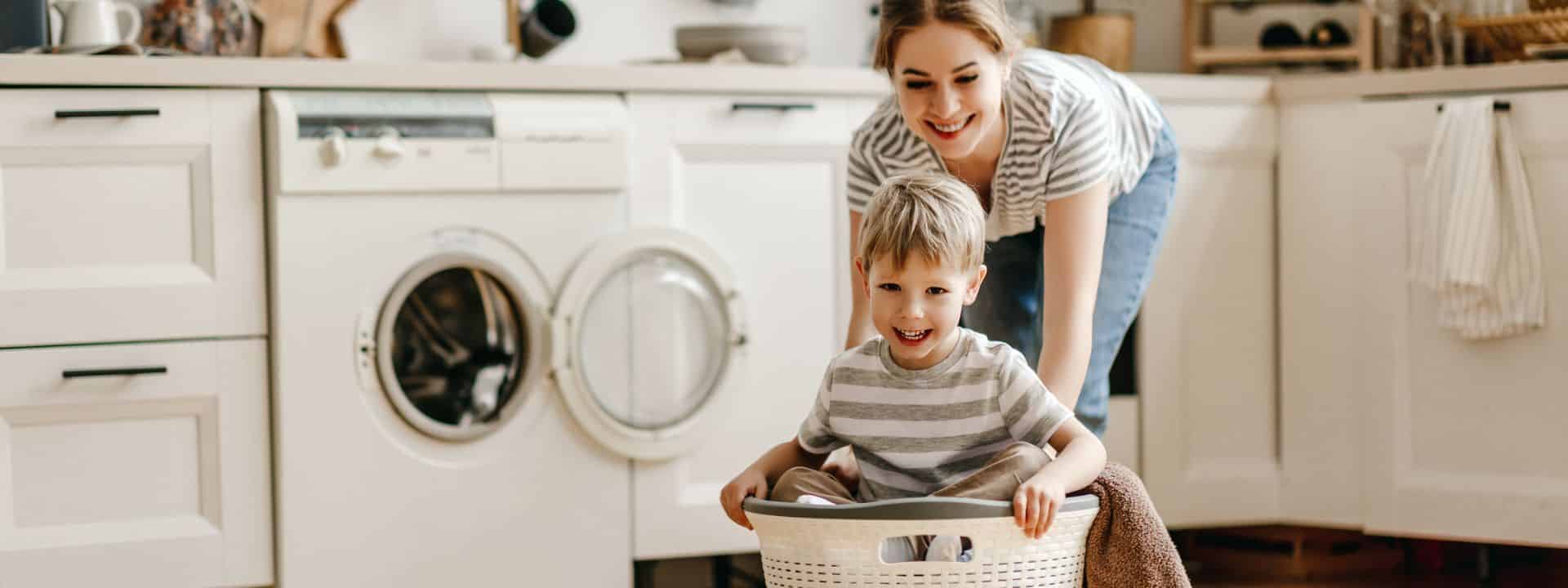 Mutter schiebt lachend ihren Sohn in einem Wäschekorb
