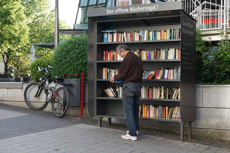 Mann liest in einem Buch an einem Tausch-Bücherregal