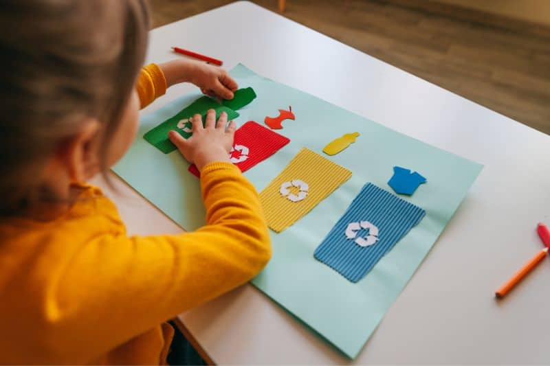 Kind klebt verschieden farbige Recyclingbehälter auf Papier