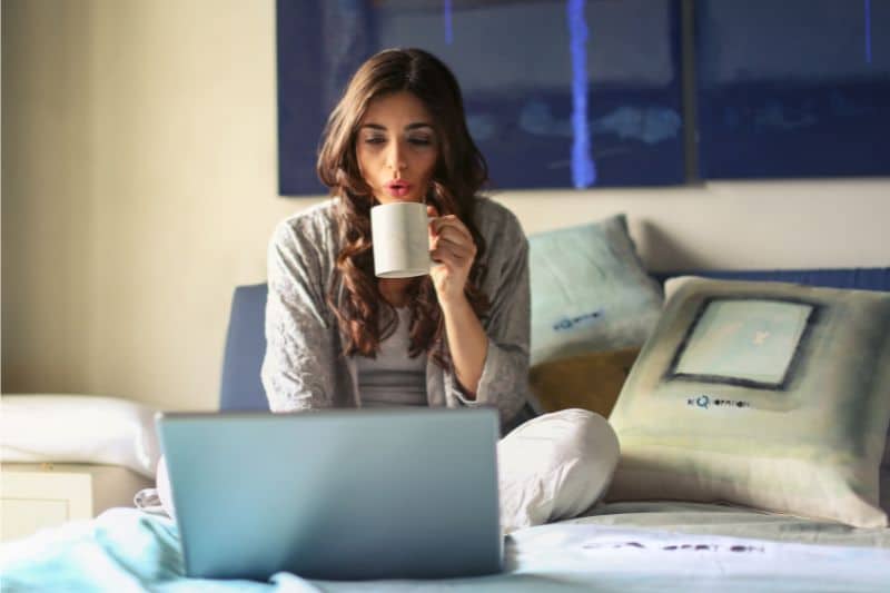 Frau sitzt vor dem Laptop und trinkt eine Tasse Kaffee
