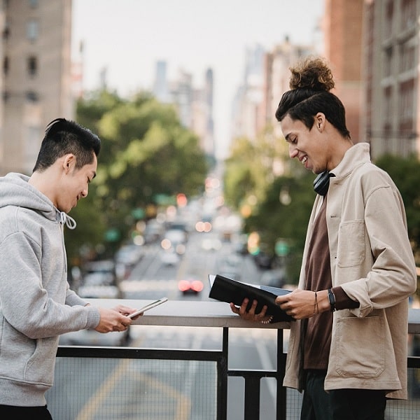 Zwei junge Männer mit einer Mappe und einem Tablet vor der Kulisse einer Stadt