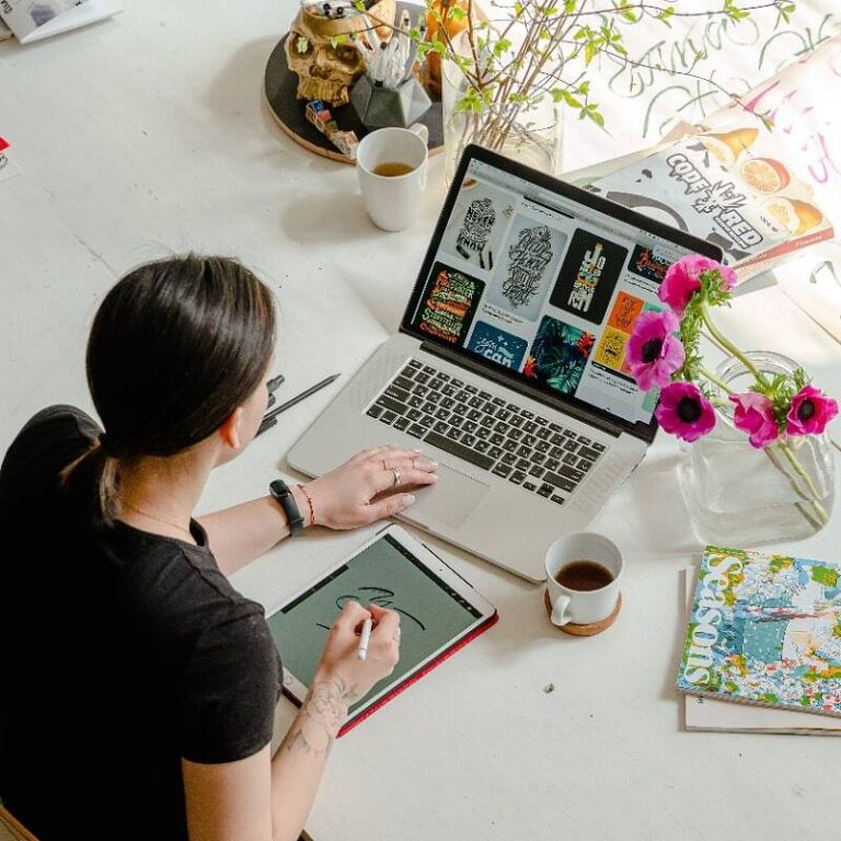Kreativer Arbeitsplatz, Schreibtisch mit bunten Accessoires, Frau öffnet Website am Laptop