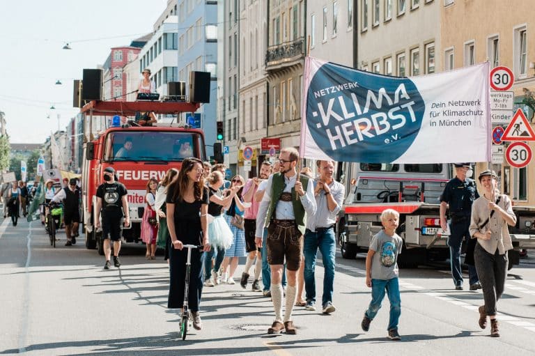Wieseneinzug des Klimaherbst München. Menschengruppe mit Plakat zum Klimaherbst